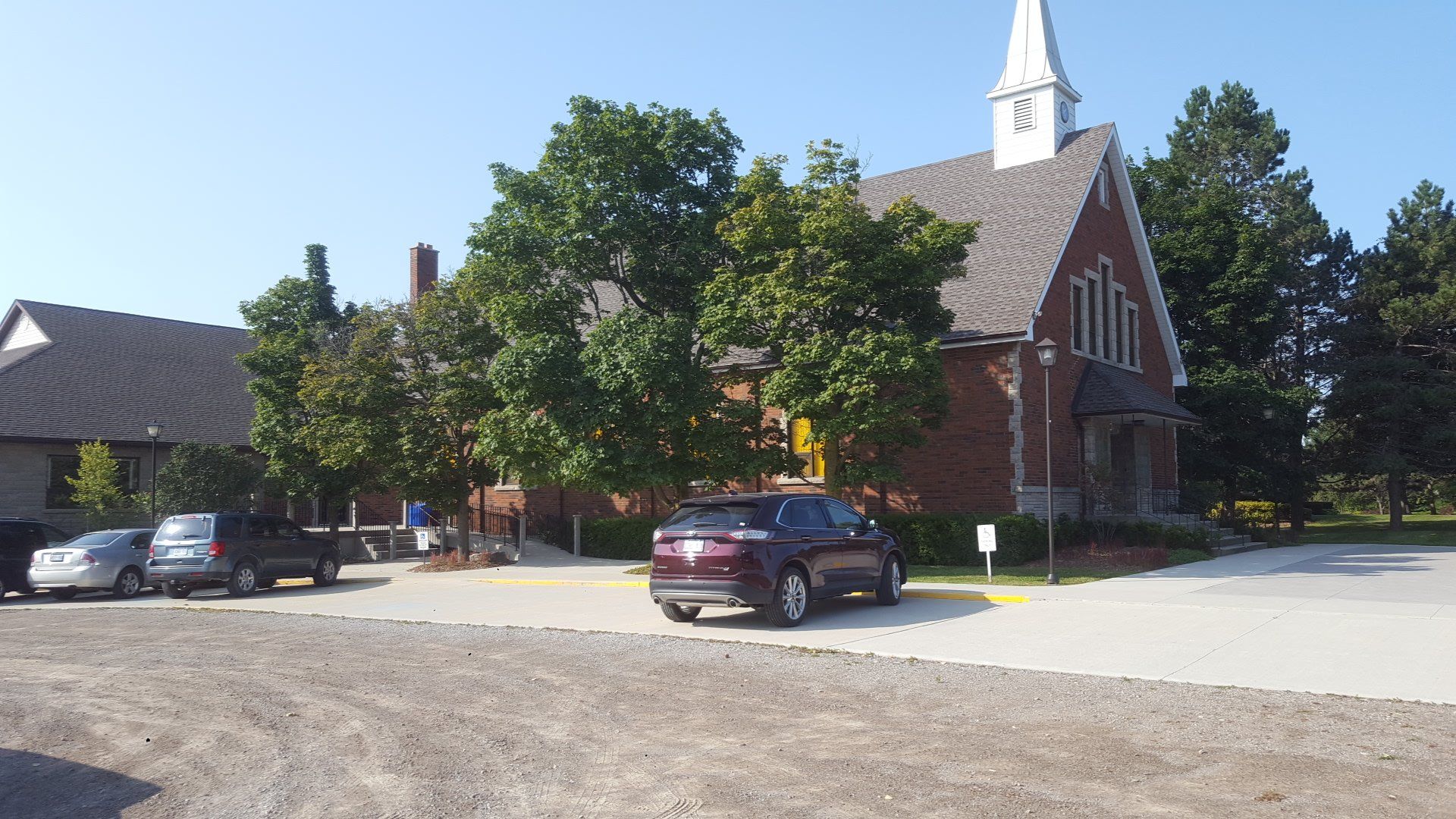 Calvin Christian Reformed Church in Dundas, a red-brick church with a white steeple and a tall window in its gable, behind trees and its parking lot