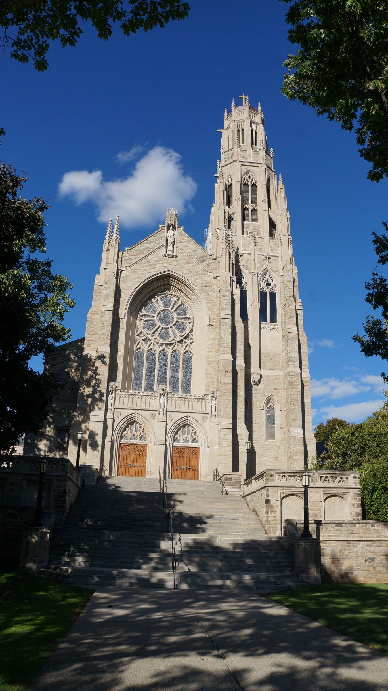 Cathedral Basilica of Christ the King, a pale stone church with a large round window above twin wooden doors and a tall pinnacled tower, seen from the foot of its broad front steps