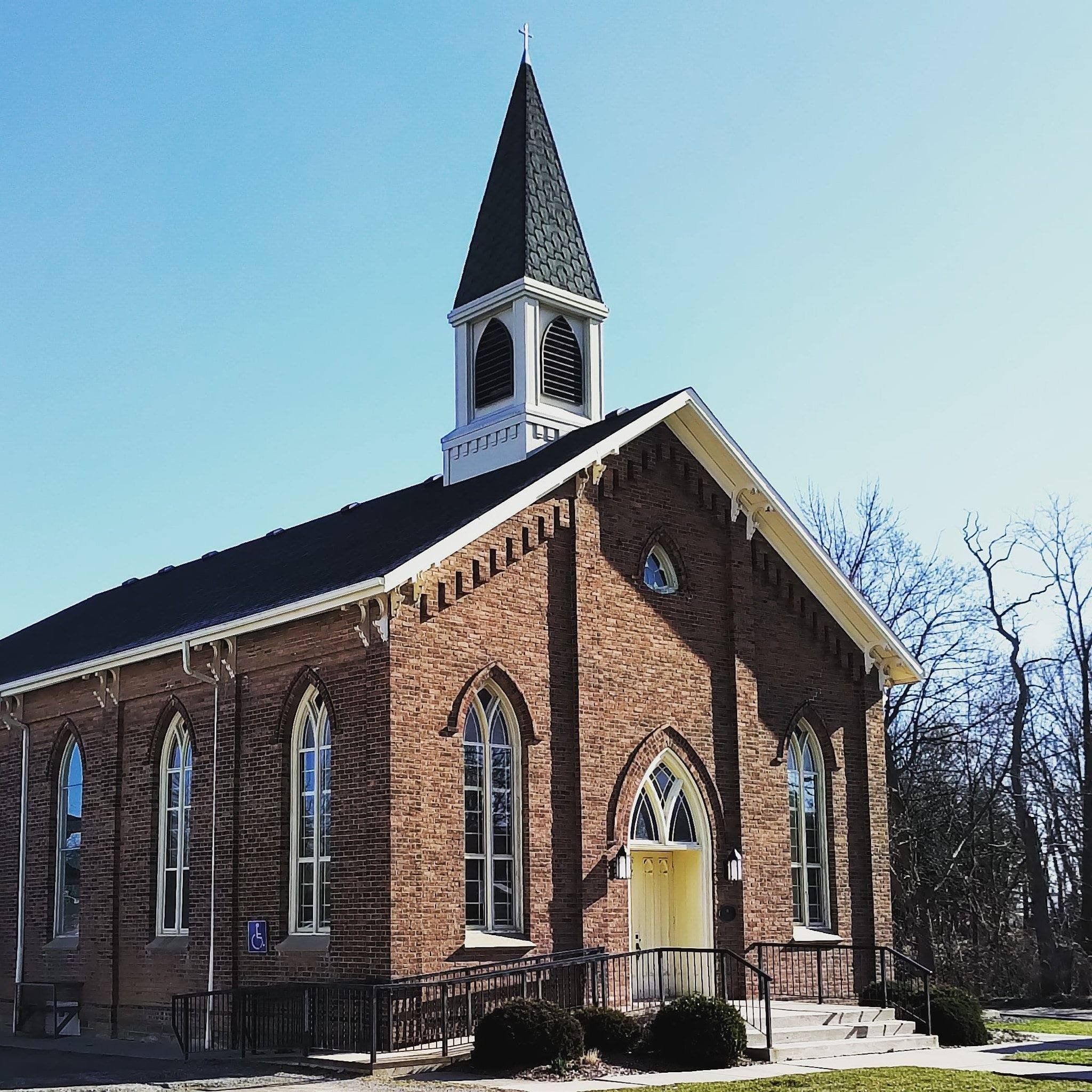 Fifty United Church, a red-brick church with tall pointed windows, a pale yellow pointed-arch front door, an access ramp and a white belfry under a dark spire