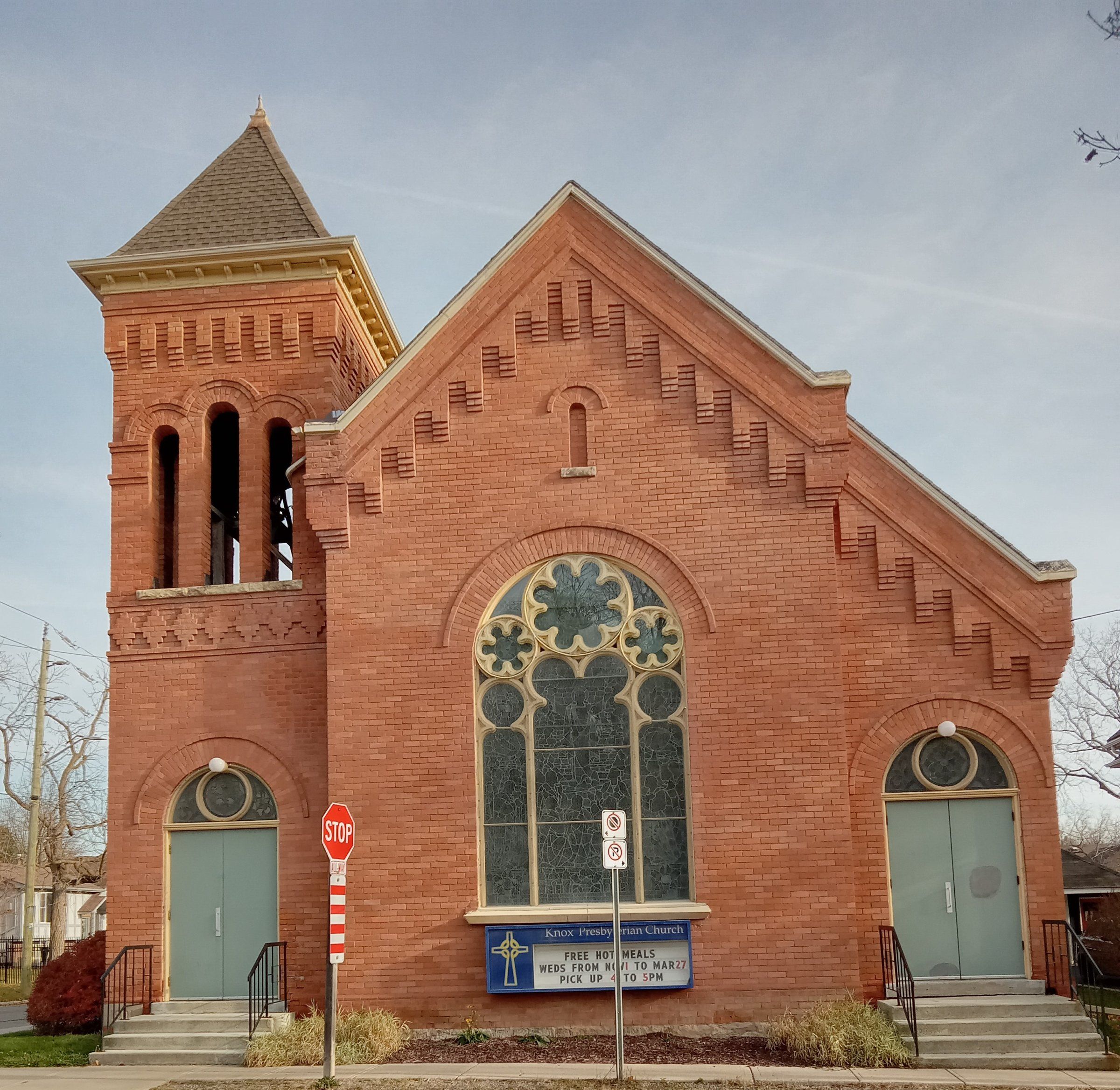 Knox Presbyterian Church, a red-brick church with a large round-arched stained-glass window between two doorways and a square bell tower with a pyramid roof, seen from the front