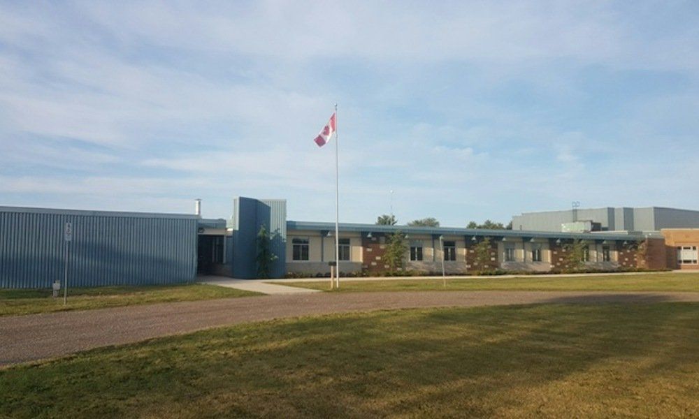 Bellstone Christian School in Mount Hope, where Living Hope meets: a long, low school building of blue and grey cladding behind a gravel drive and a lawn, with a Canadian flag on a tall pole