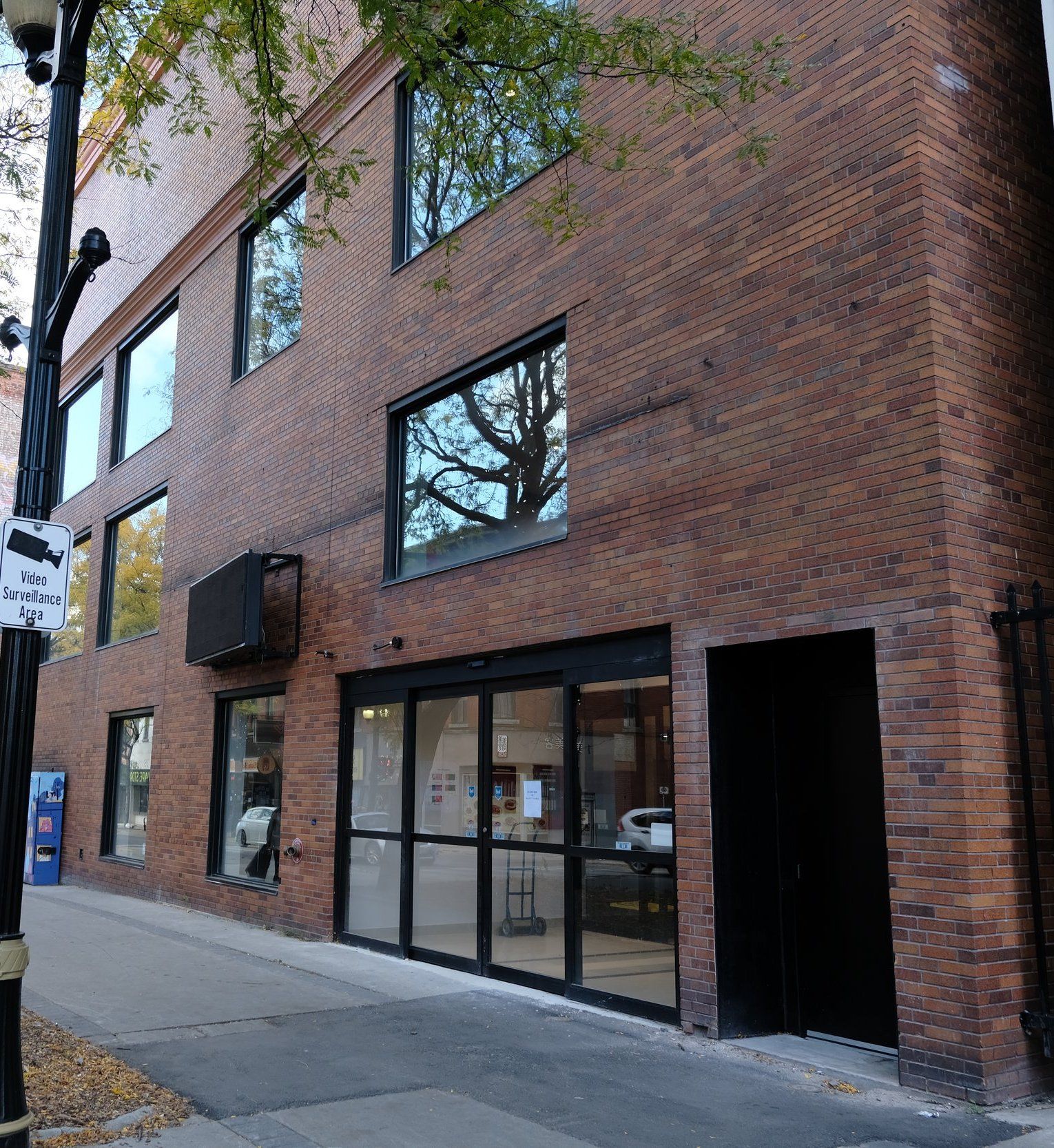 Philpott Church, a three-storey red-brick building with large black-framed windows and a row of glass entrance doors, beside a tree-lined downtown sidewalk