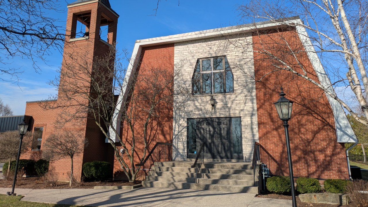 Providence Canadian Reformed Church, a red-brick church whose pale stone front frames a tall window and double doors at the top of a broad flight of steps, with a square brick bell tower at the left, under a clear blue sky