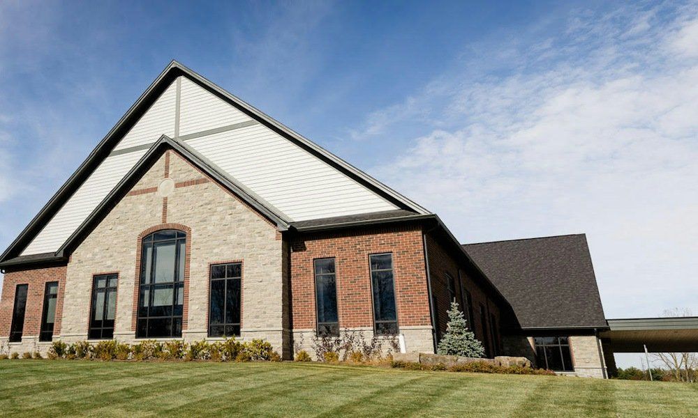 Redemption Canadian Reformed Church, a new church whose broad gable of pale stone and white siding frames a tall arched window, with red-brick walls running back beside a mown lawn