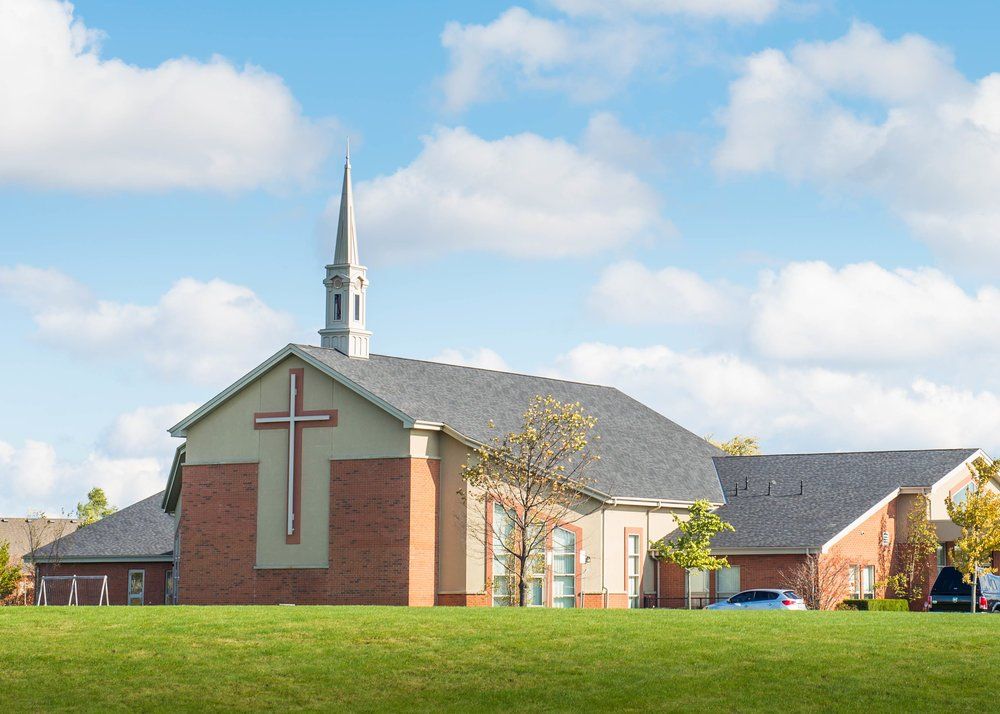 Rehoboth United Reformed Church, a red-brick church with a pale upper gable set with a tall cross, a white steeple and lower brick wings, seen across a wide lawn