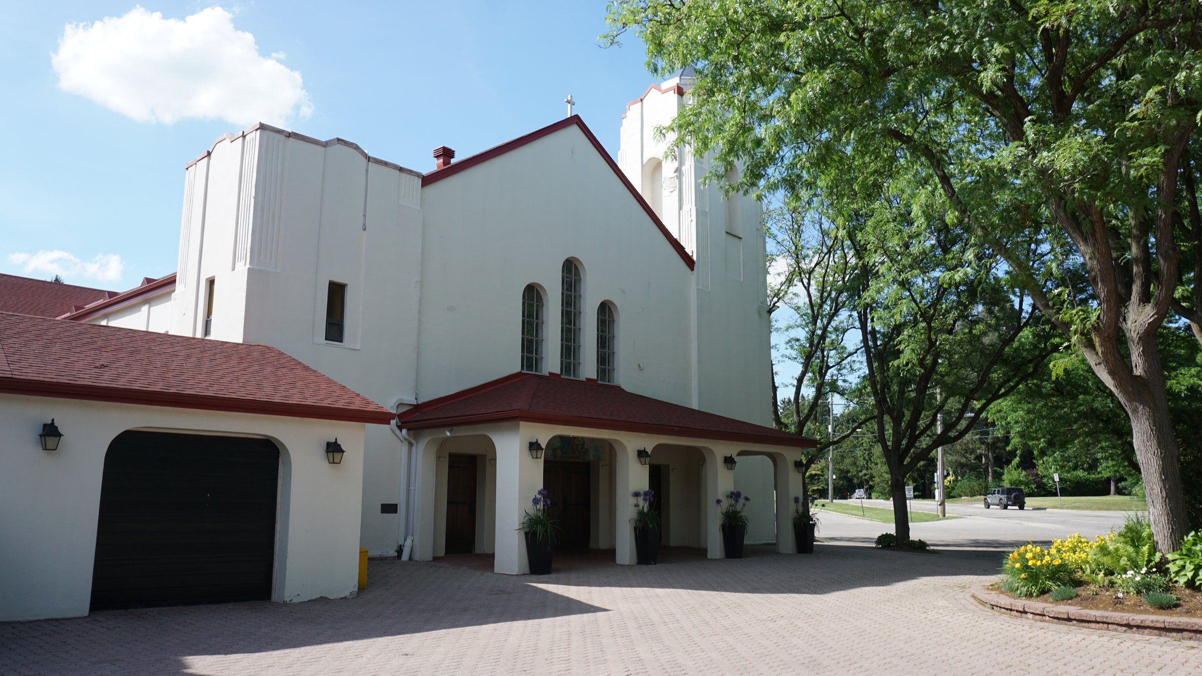 St. Ann Church, a white stucco church with red roofs and three tall arched windows above an arched front porch, with a white bell tower partly hidden by a tree