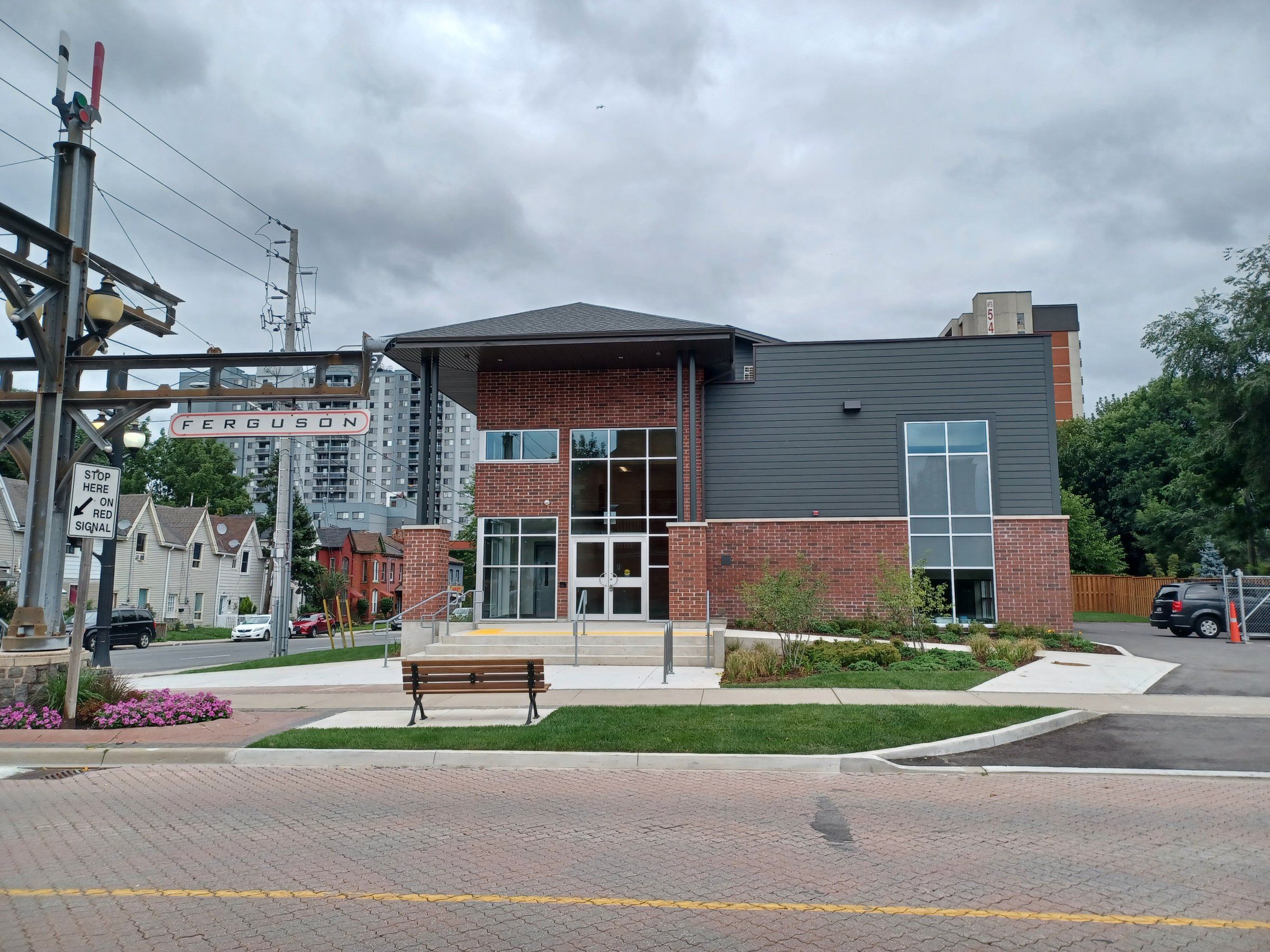 Streetlight Christian Church, a two-storey building of red brick and grey siding with a tall glazed entrance, seen across a brick-paved street, a bench and flower beds on Ferguson Avenue North