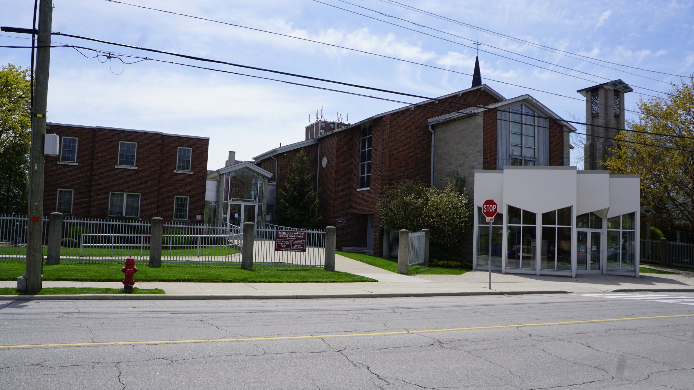 Sts. Peter and Paul Church, a red-brick church with a stone and glass front gable, a small spire and a tall open bell tower, with a white glass-walled entrance in front and a two-storey brick building beside it, seen across Brucedale Avenue East