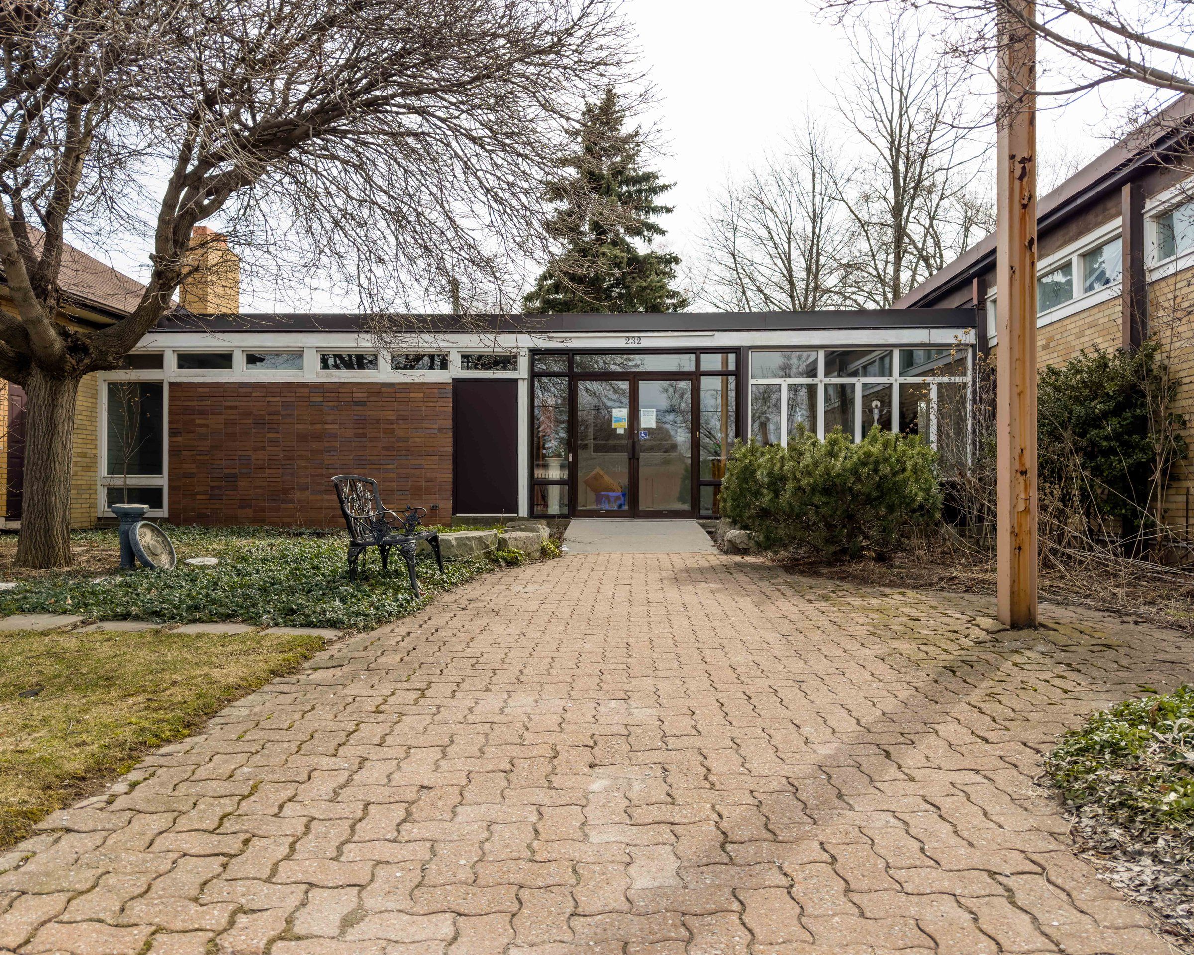 The entrance at 232 Fennell Avenue East, where Trinity Lutheran worships while its own church is renovated: a low glass-and-brick link between yellow-brick wings, at the end of a brick-paved walk
